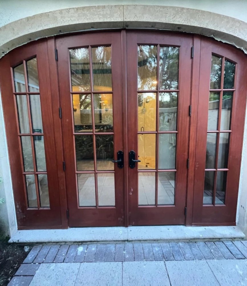 Arched mahogany French doors with divided glass lites and matching arched sidelights set into a stone surround