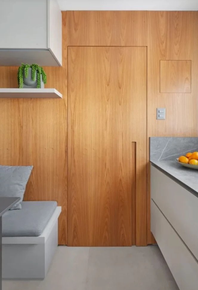 Concealed door clad in the same oak panelling as the surrounding kitchen wall, with a recessed vertical pull