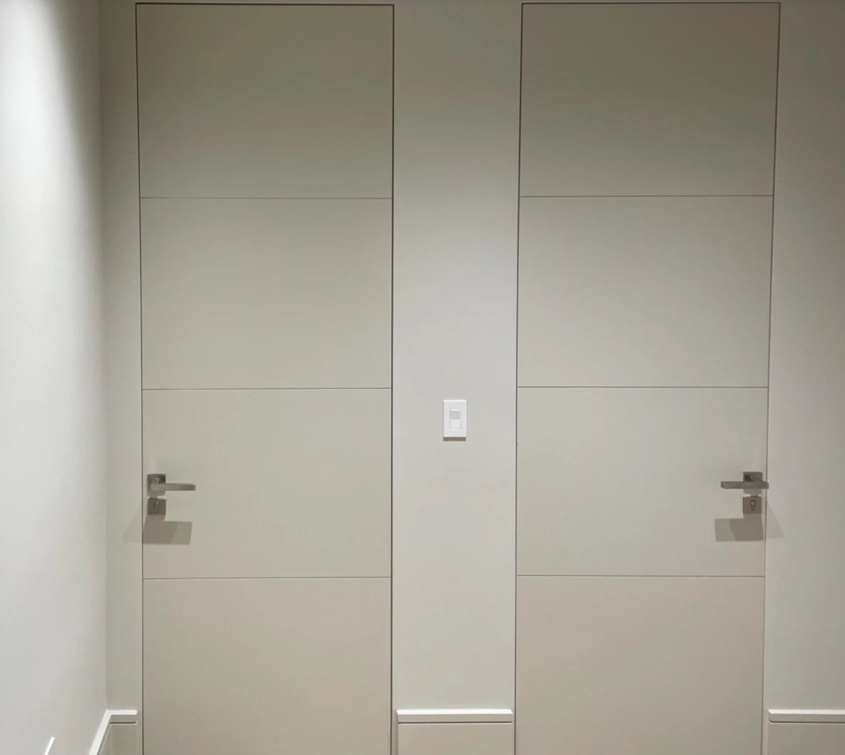 Pair of flush painted interior doors with horizontal grooves and slim lever handles, set flush with the wall