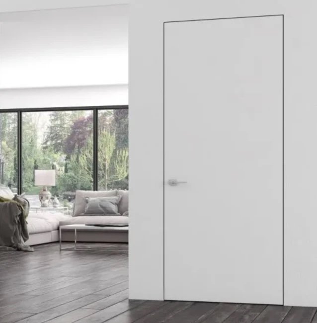 Frameless matte white interior door set flush in a white wall beside a bright living room