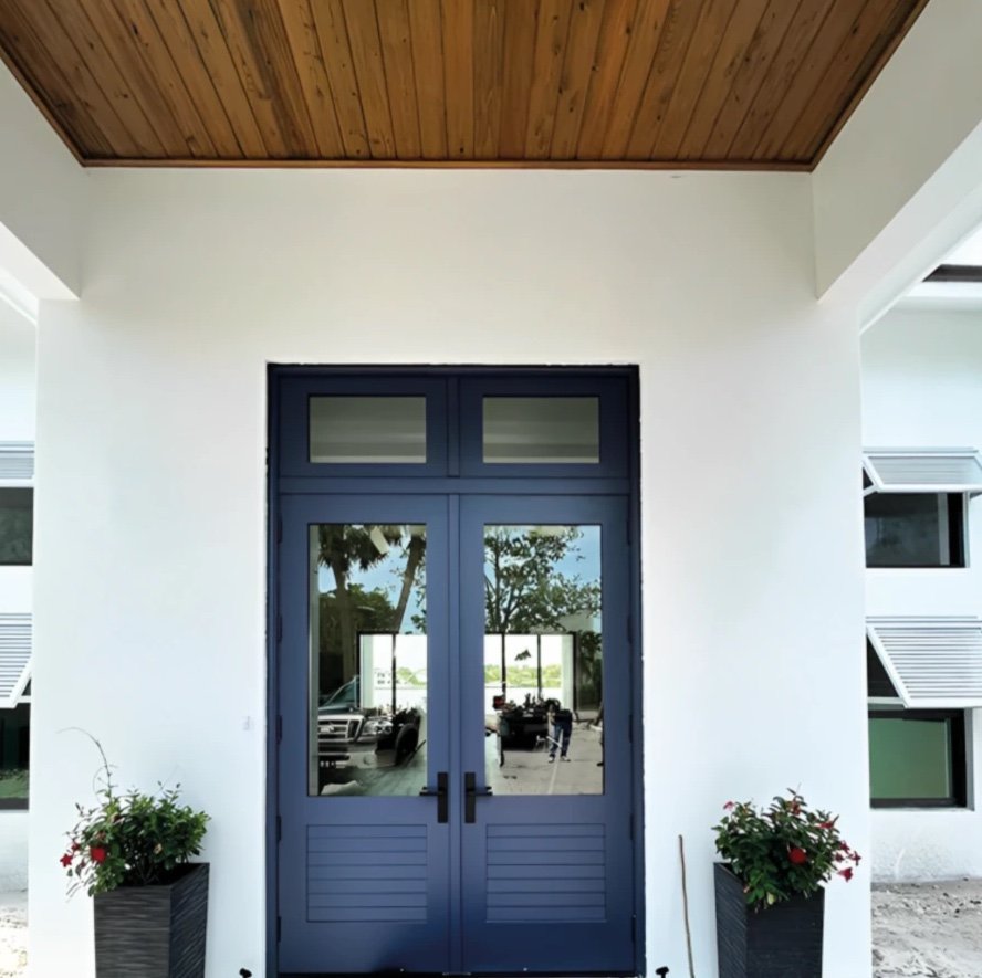 Navy double entry doors with large glass lites, louvered lower panels and a frosted transom under a timber porch ceiling