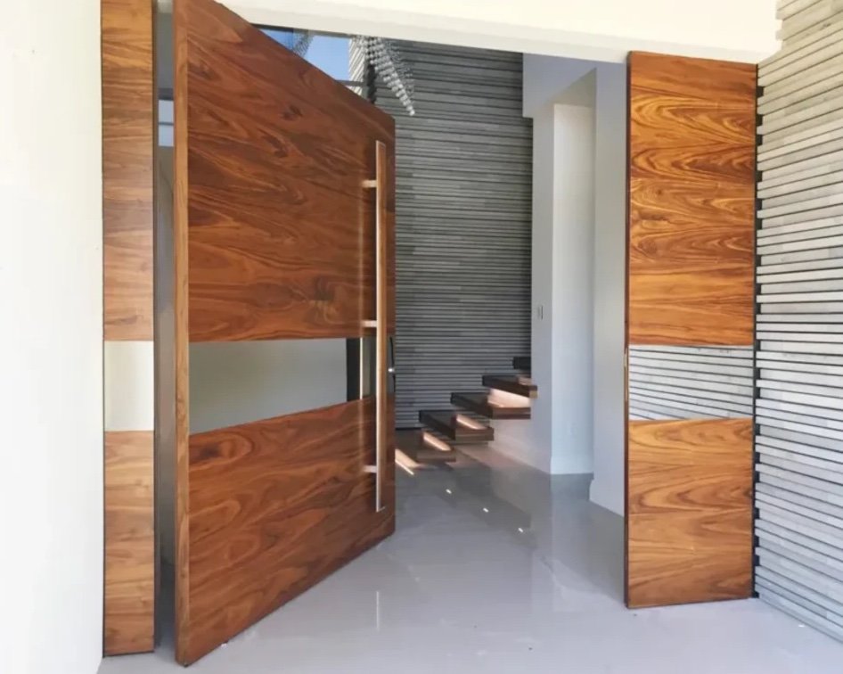 Figured hardwood pivot doors with a frosted glass band opening onto a floating staircase